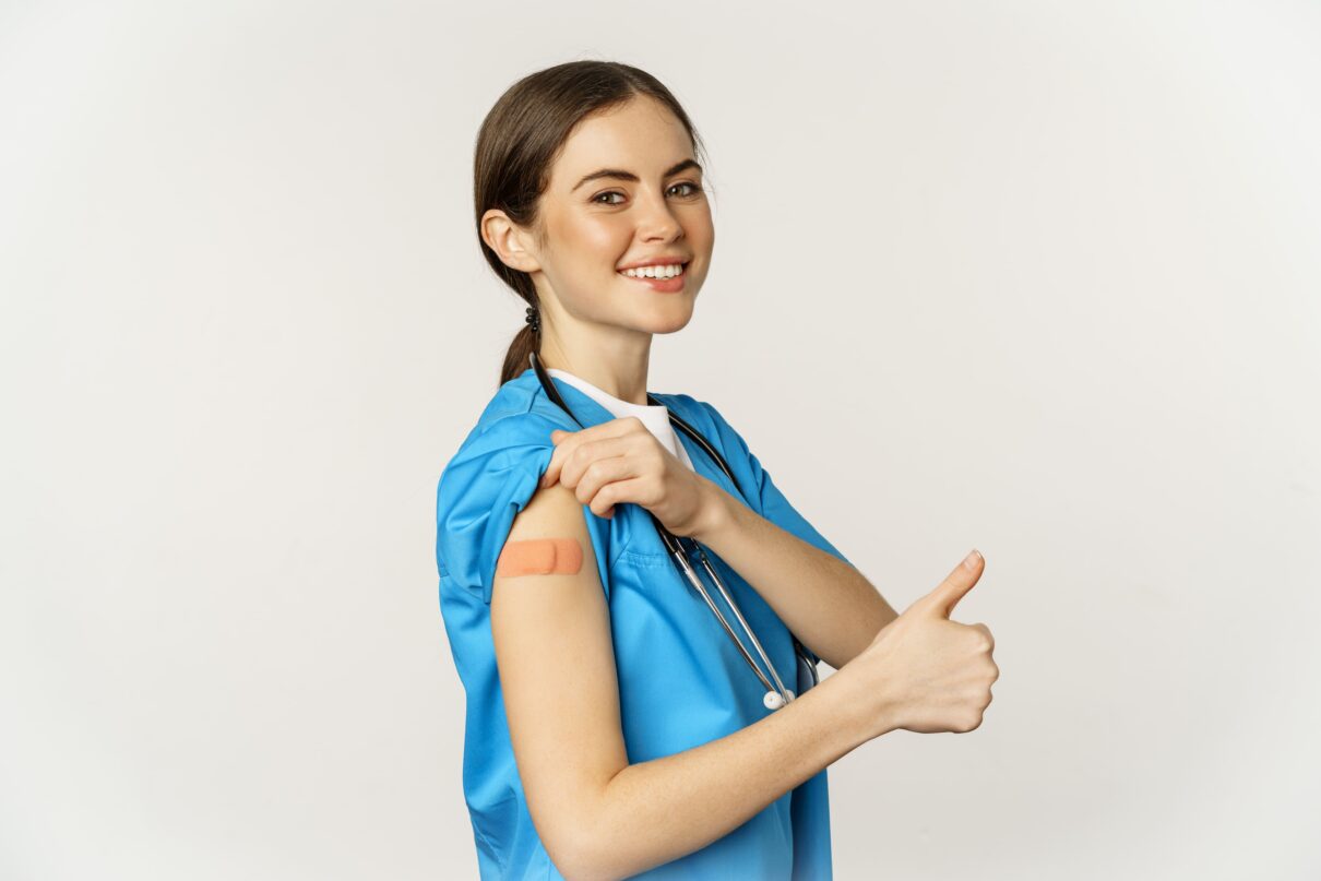 smiling nurse medical worker showing thumbs up shoulder after taking women vaccines standing white background scrubs