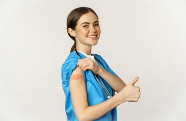 smiling nurse medical worker showing thumbs up shoulder after taking women vaccines standing white background scrubs