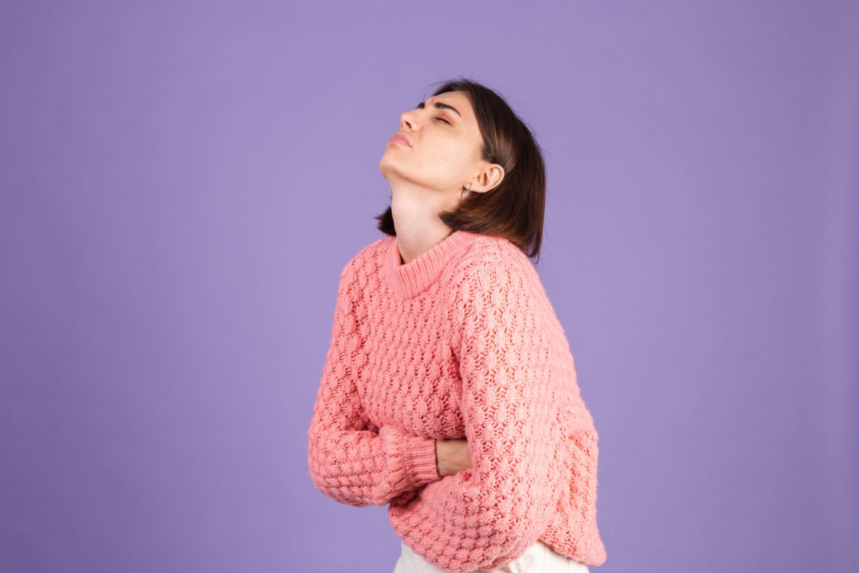 young woman wearing pink sweater having a Women’s UTI & Allergy and she isolated purple wall
