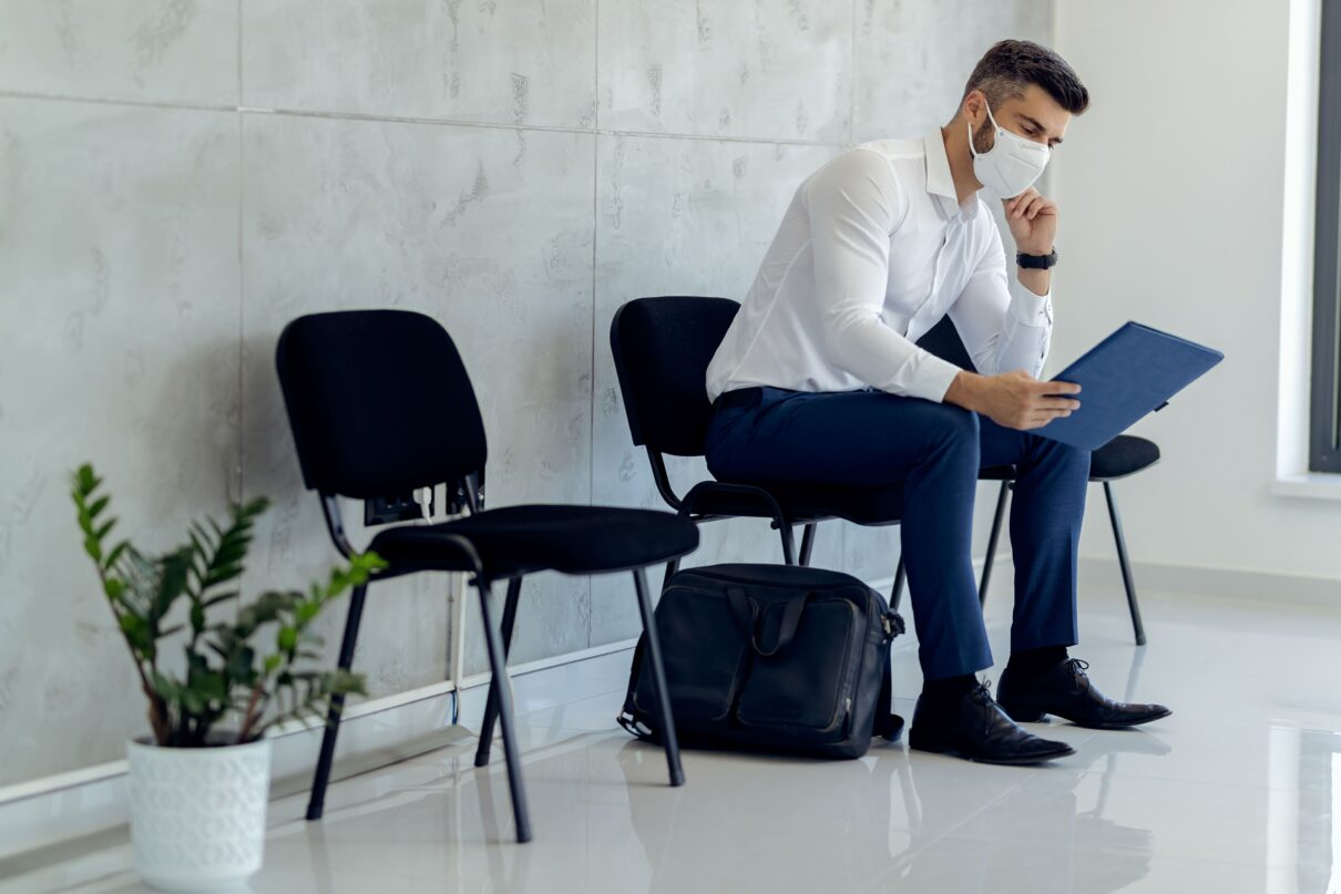 businessman wearing protective face mask while waiting pre-employment physical exam