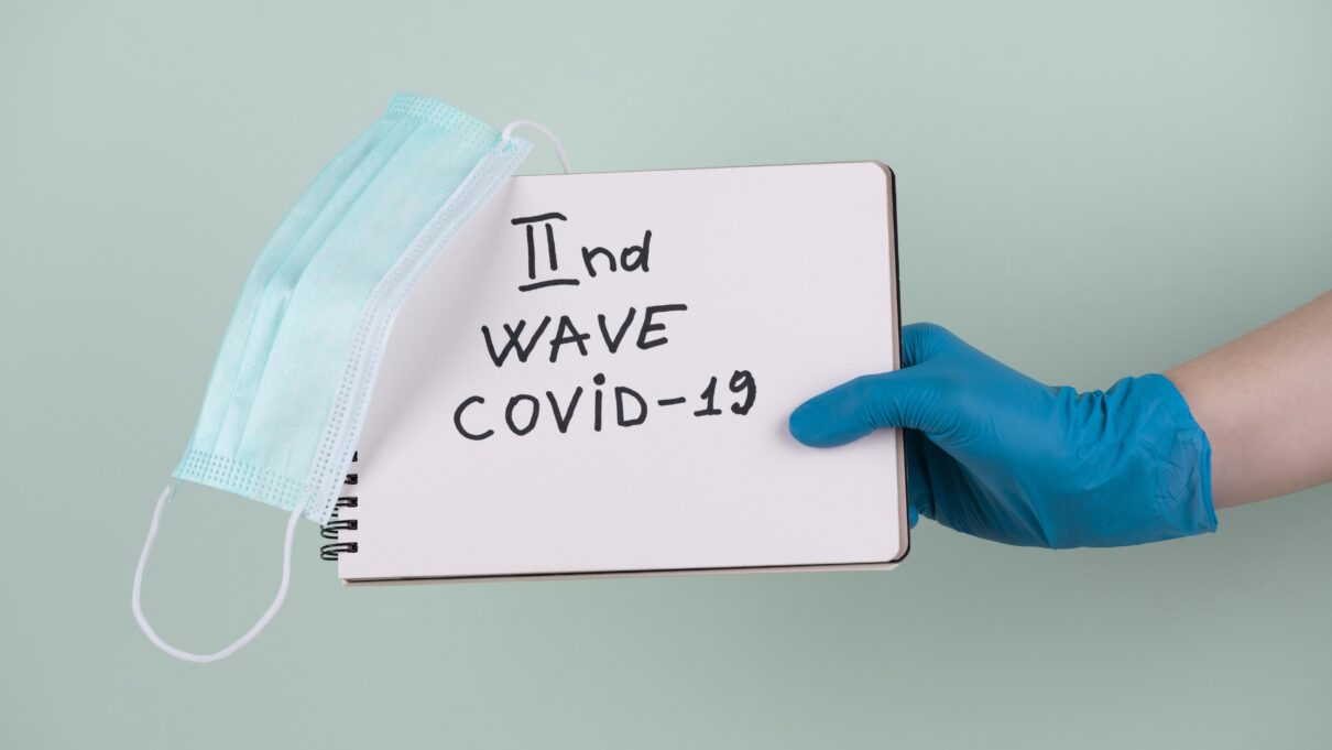 hand with surgical glove holding notebook saying second wave covid With a mask on the notebook expressing flu COVID prevention tips