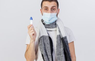 looking camera young ill man wearing medical mask scarf holding thermometer isolated white to warn against subclade K flu strain